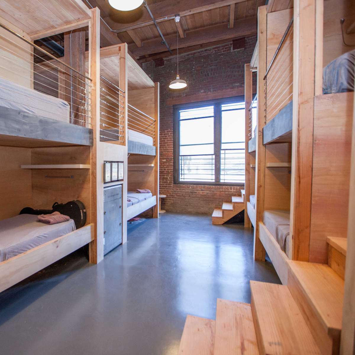 A modern bunk room with wooden bunk beds and a large window allowing natural light to enter.