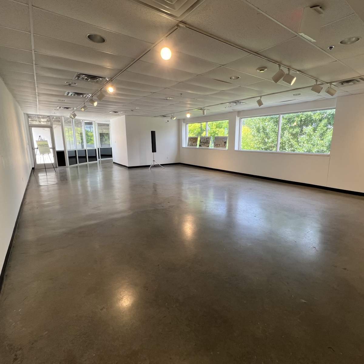An empty, well-lit gallery space with large windows and polished concrete flooring.