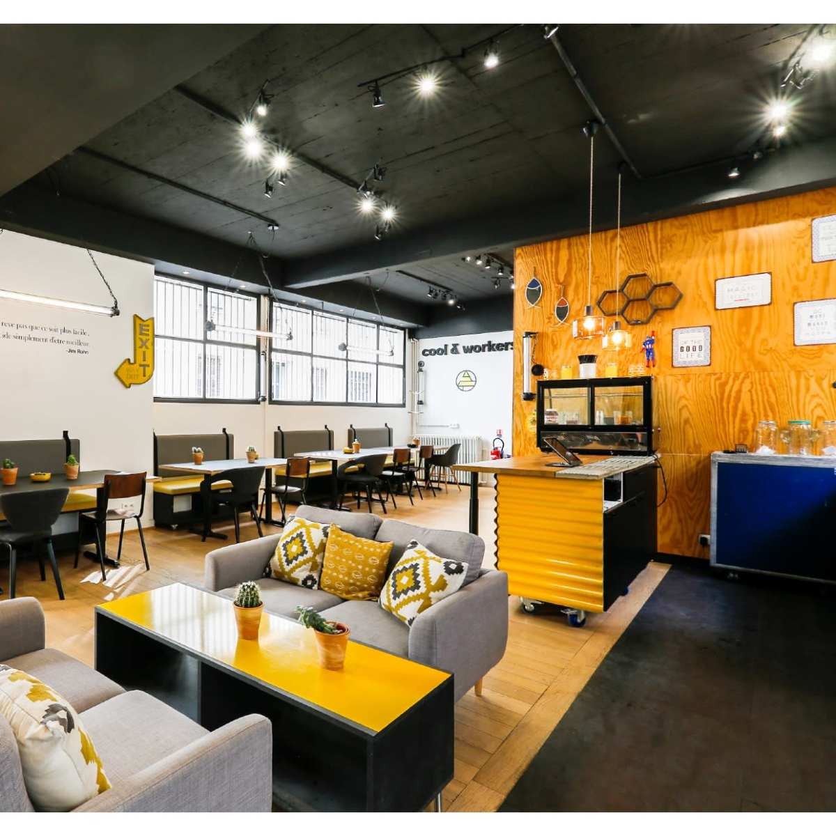 A modern café interior with seating areas, a service counter, and decor featuring wooden panels and bright yellow accents.