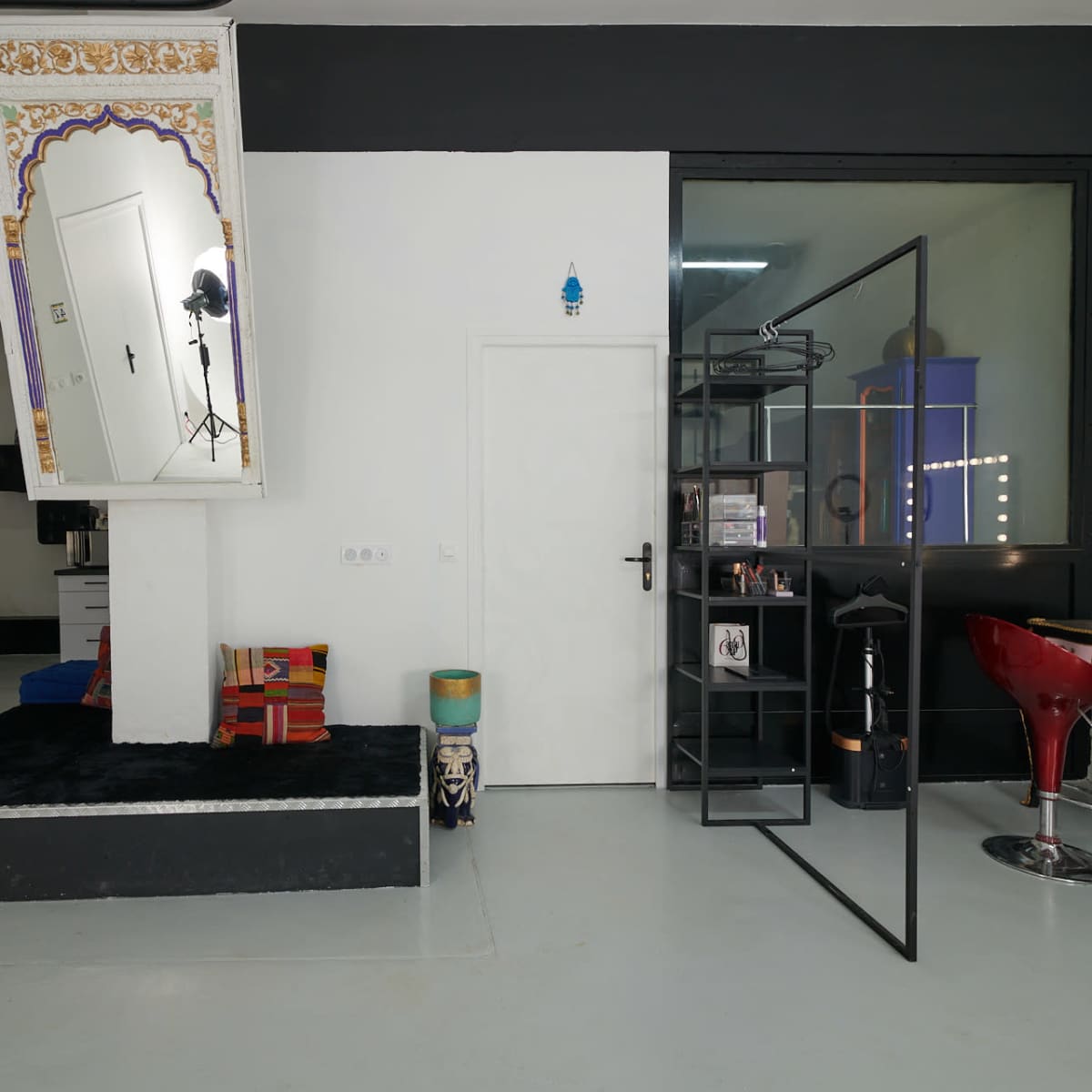 A modern interior space featuring a mix of furniture and decor, including a mirrored wall, a black shelving unit, and a lit vanity area.