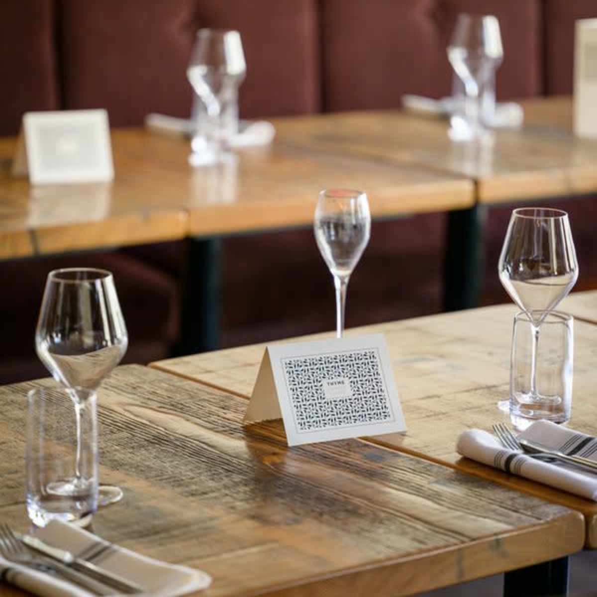 A dining setup with wooden tables, each featuring glasses and a folded menu card at the center.