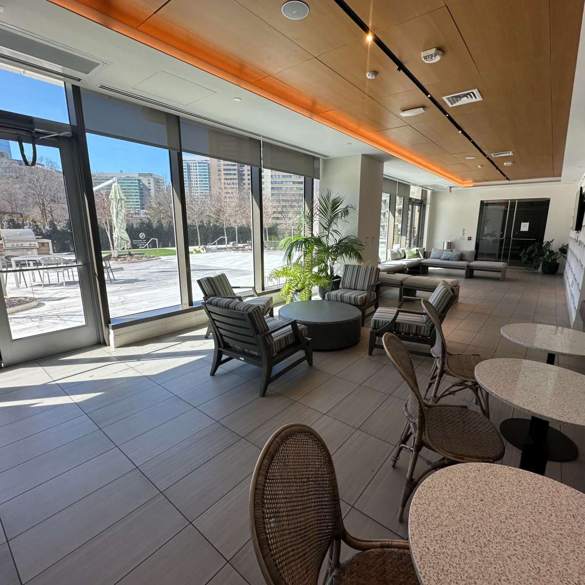 A modern lounge area with comfortable seating, large windows, and a view of an outdoor patio space.
