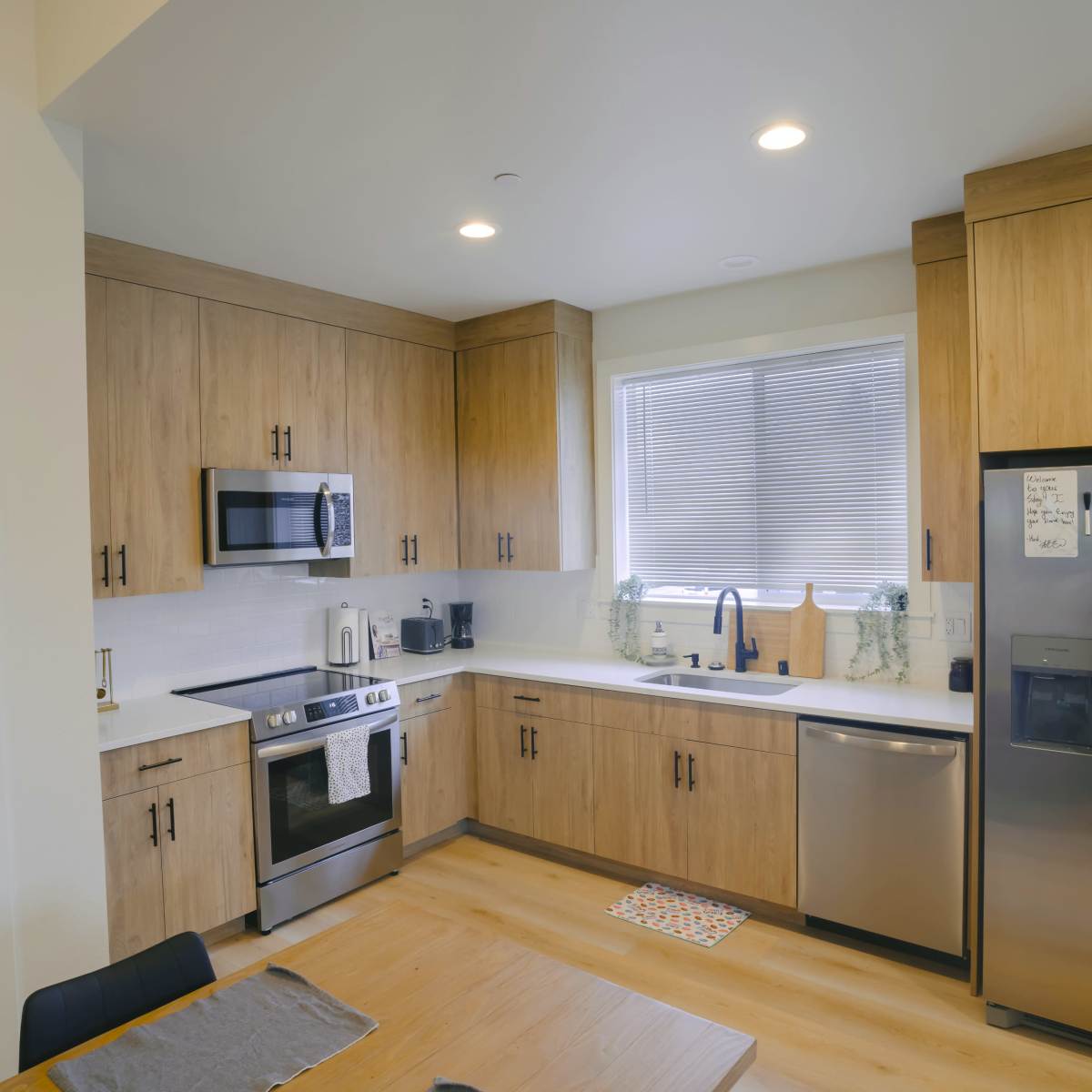 A modern kitchen with wooden cabinets, stainless steel appliances, and a window above the sink.