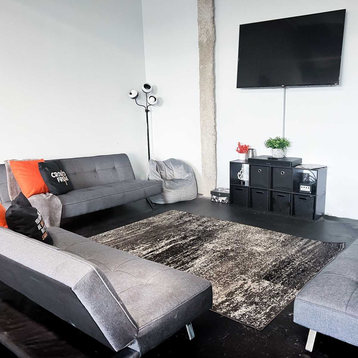 A modern living space with two gray sofas, a large area rug, a wall-mounted television, and a set of black storage units.