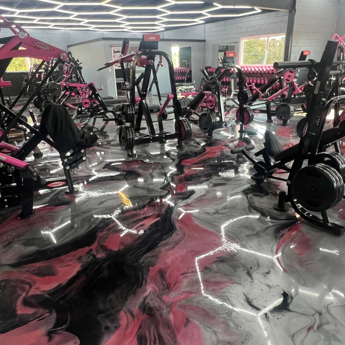 A gym interior with exercise equipment arranged around a black and pink marbled floor.