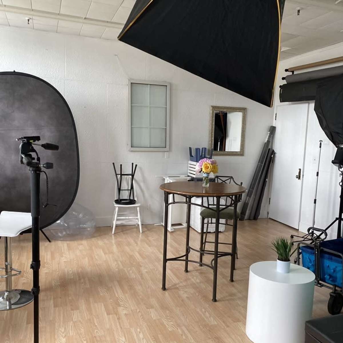 A photography studio with various equipment, a small round table with a flower vase, and a couple of chairs.