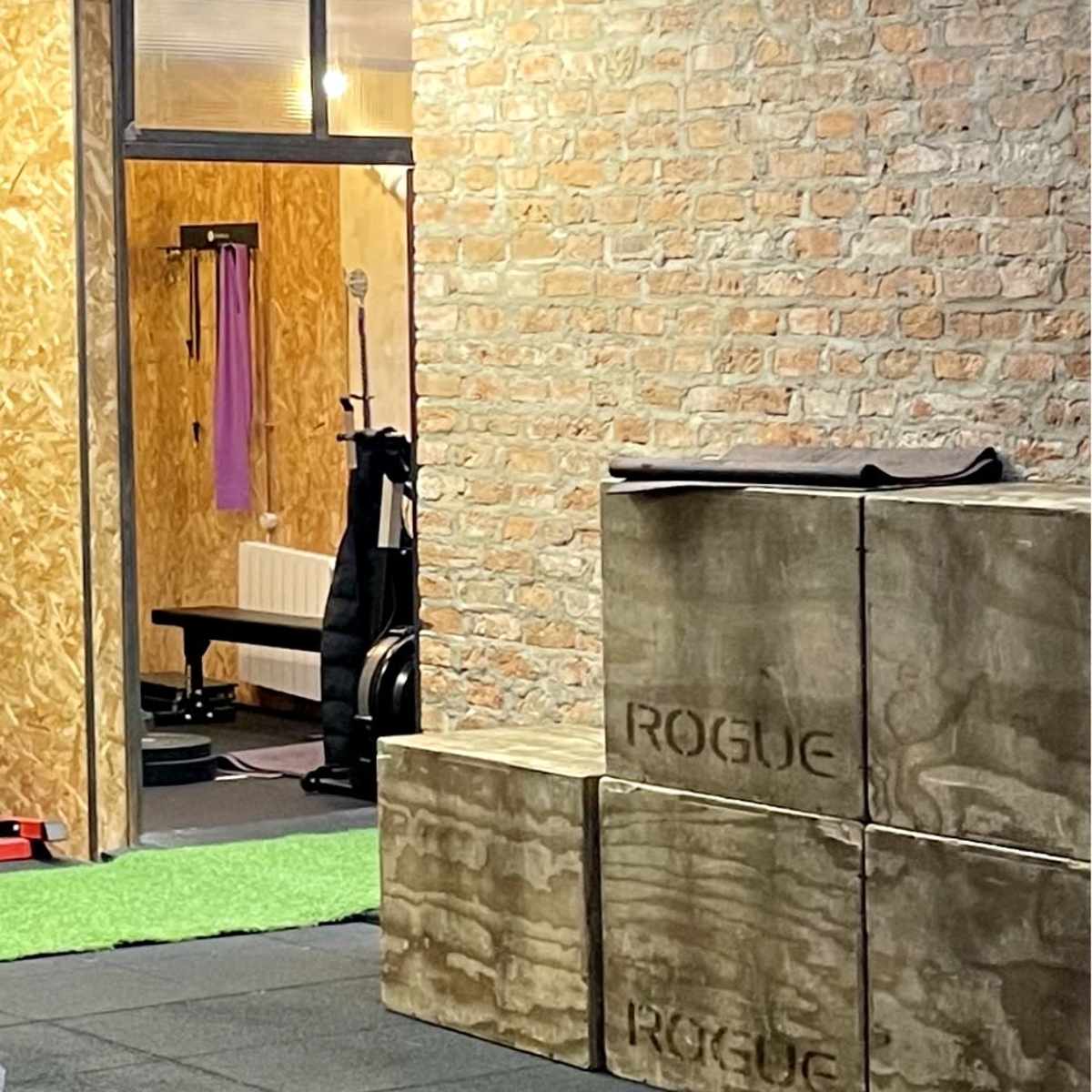 A workout space with concrete blocks labeled "ROGUE," a green turf area, and a wooden wall.