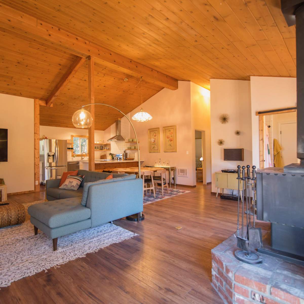 A spacious living area with a wooden ceiling, a television on the wall, and furniture arranged around a central rug.