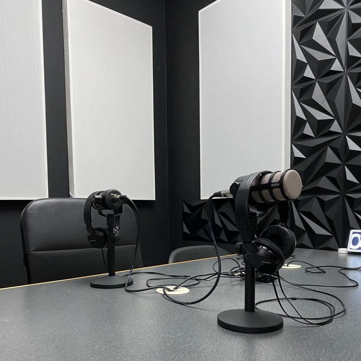 A podcast recording studio with two microphones on stands, a pair of headphones, and soundproof wall panels.