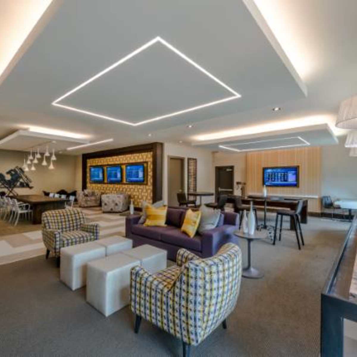 A modern lounge area featuring seating arrangements, flat-screen displays, and ambient lighting.