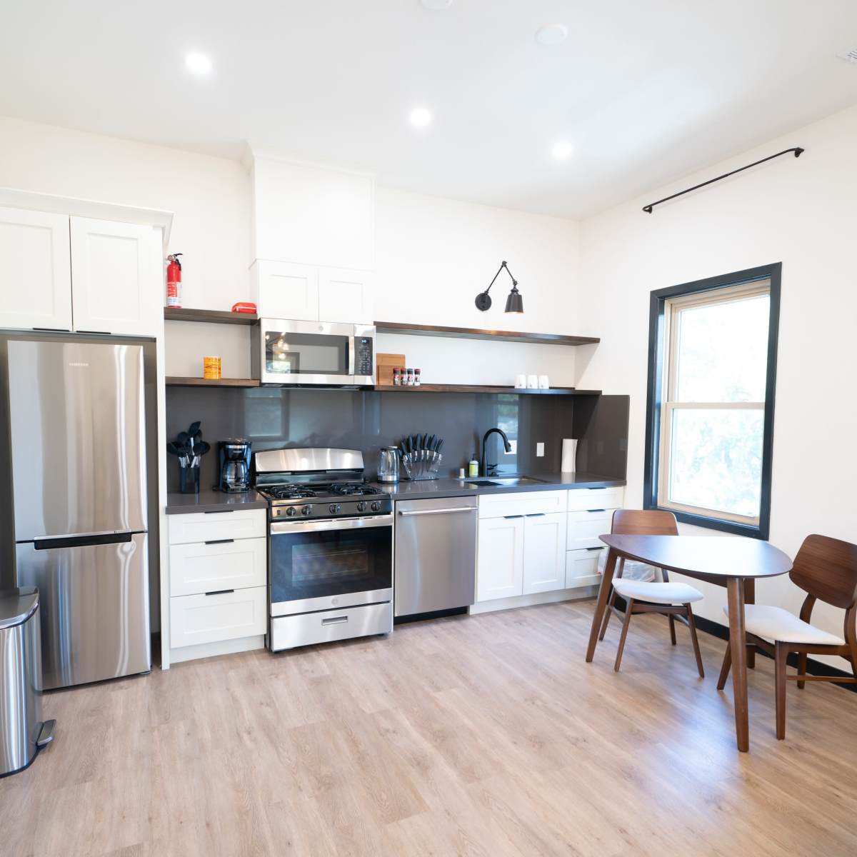 A modern kitchen with stainless steel appliances, white cabinetry, and a wooden dining table.