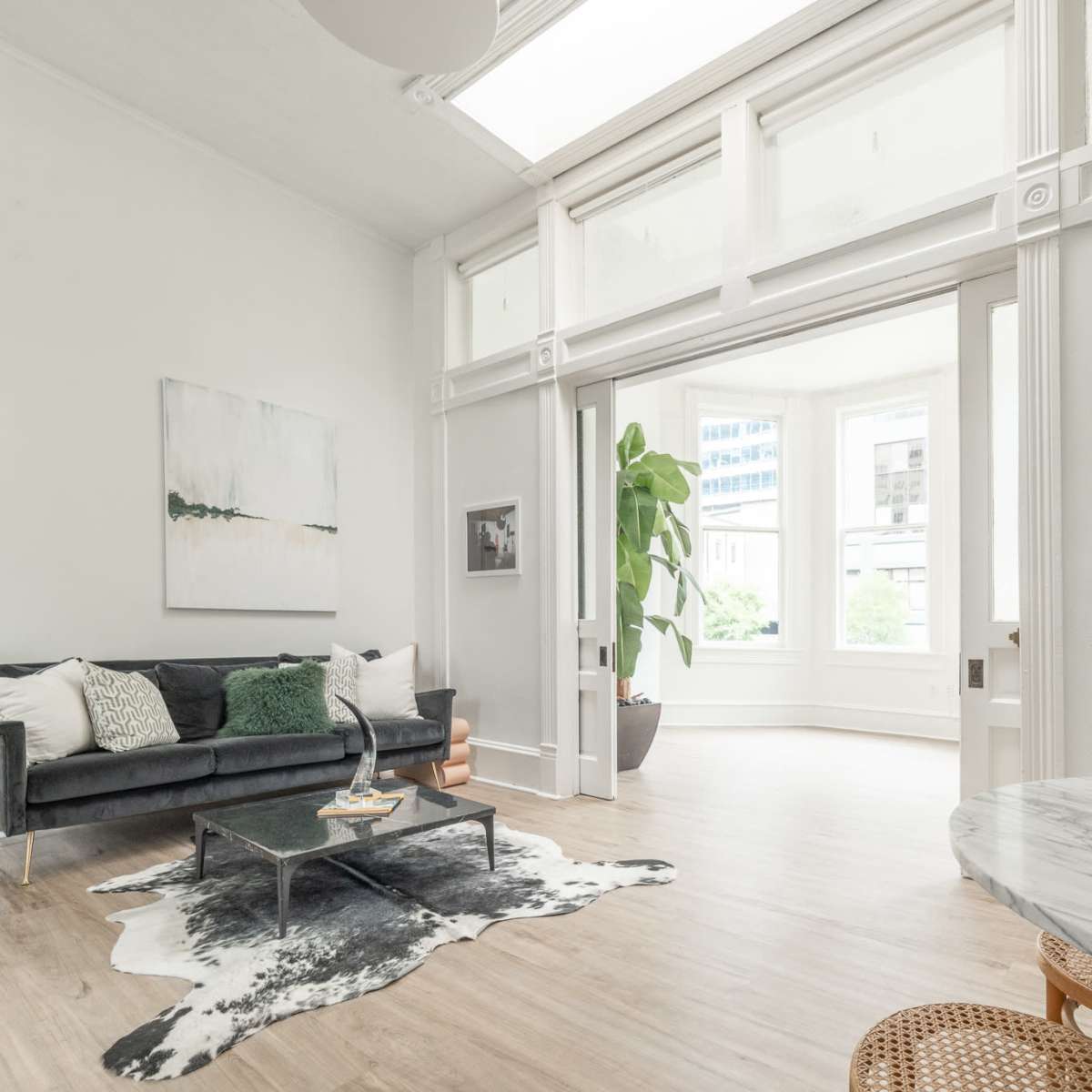 A bright living room features a green sofa, a round marble table, and large windows that allow ample natural light.