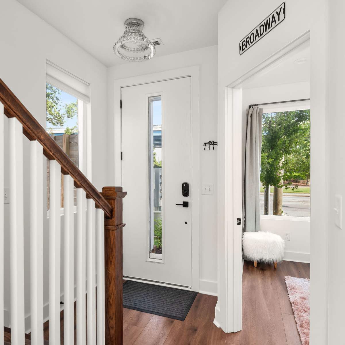 A well-lit entryway with a staircase on the left, a front door at the center, and a window with a view of the outdoors on the right.