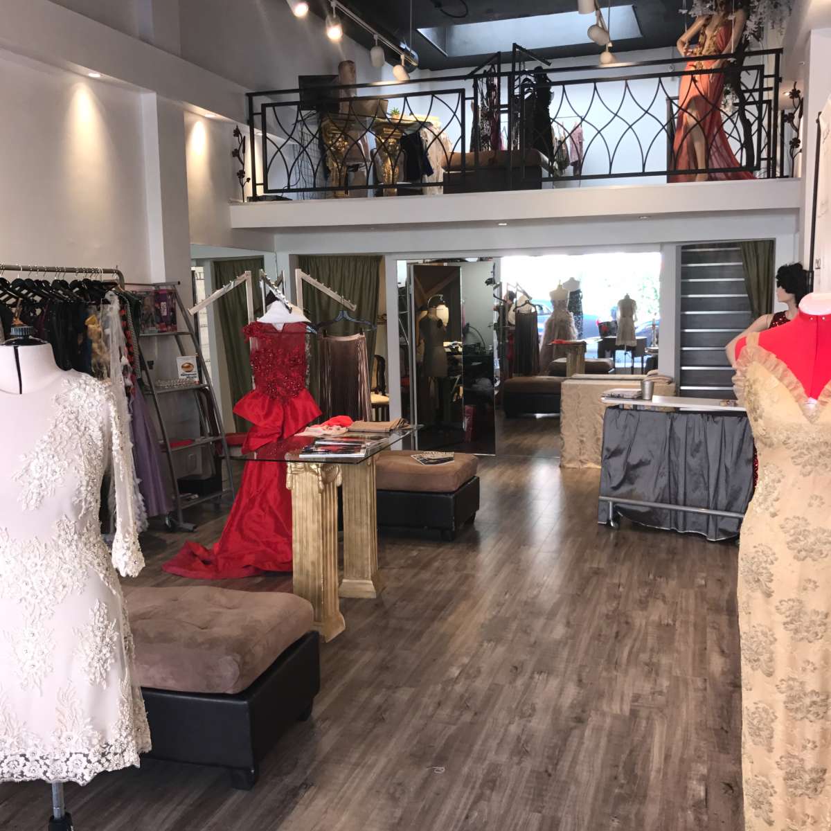 A boutique interior featuring a variety of elegant dresses displayed on mannequins and clothing racks, with a staircase leading to an upper level.
