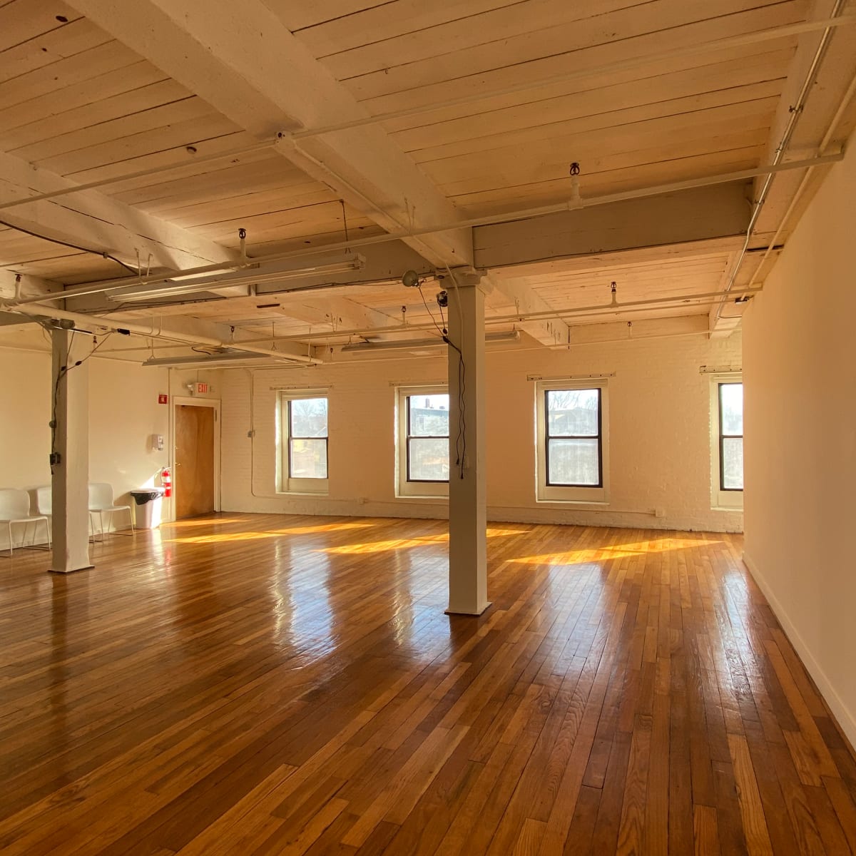 A spacious, empty room with hardwood floors and several large windows letting in natural light.