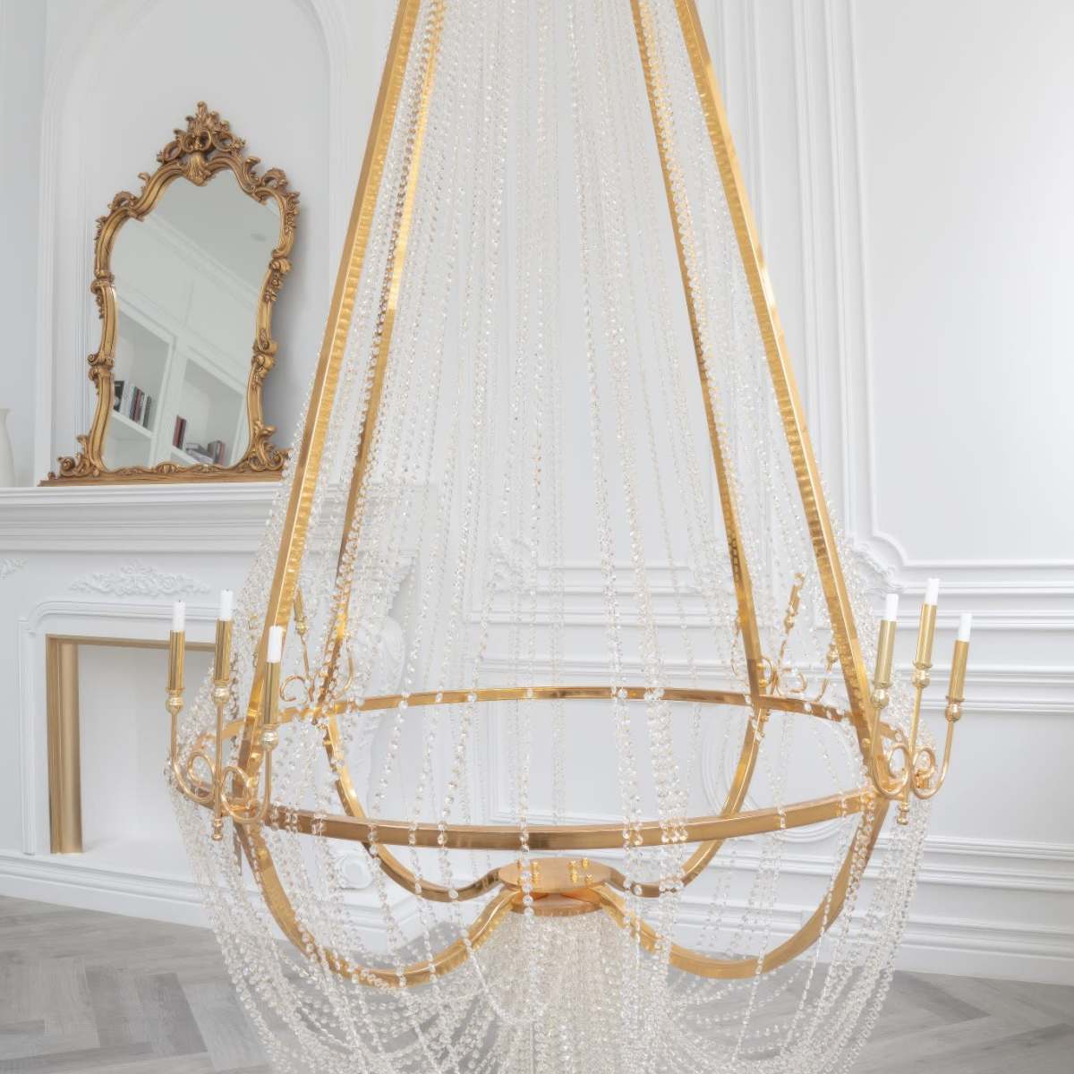 A large, gold and crystal chandelier hangs from the ceiling in a bright, elegantly decorated room with white walls and ornate moldings.