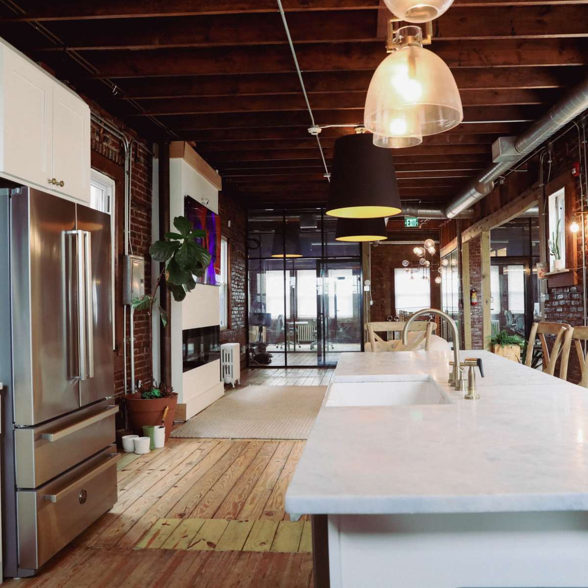 A modern kitchen features a large white countertop island, stainless steel appliances, and exposed wooden beams.