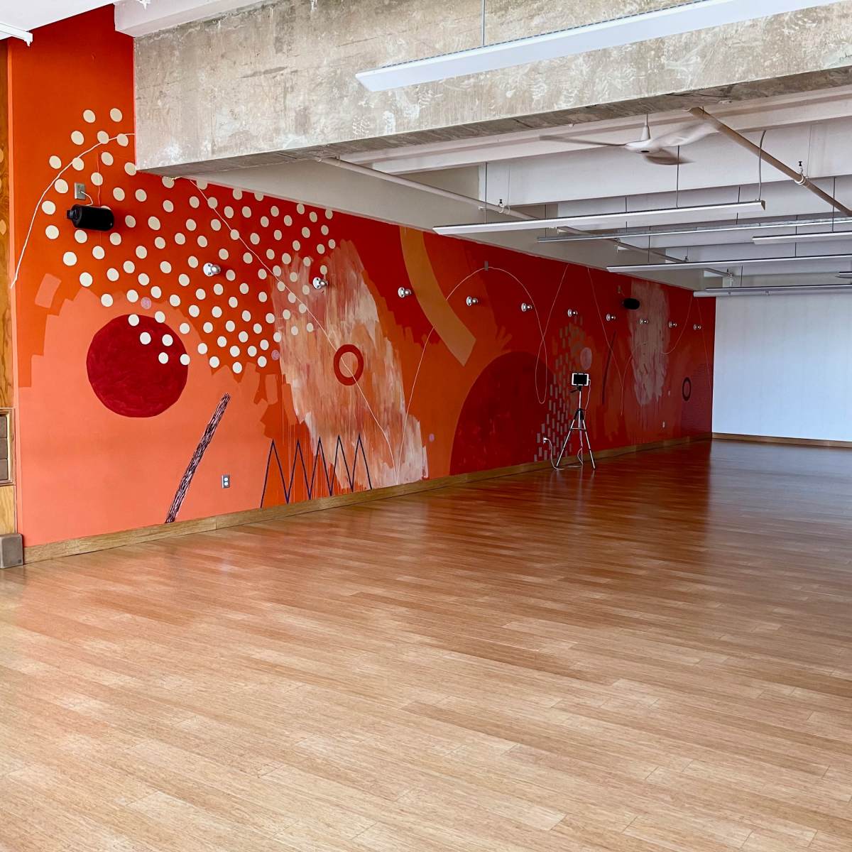 A spacious, empty room with wooden flooring and an orange mural on one wall.