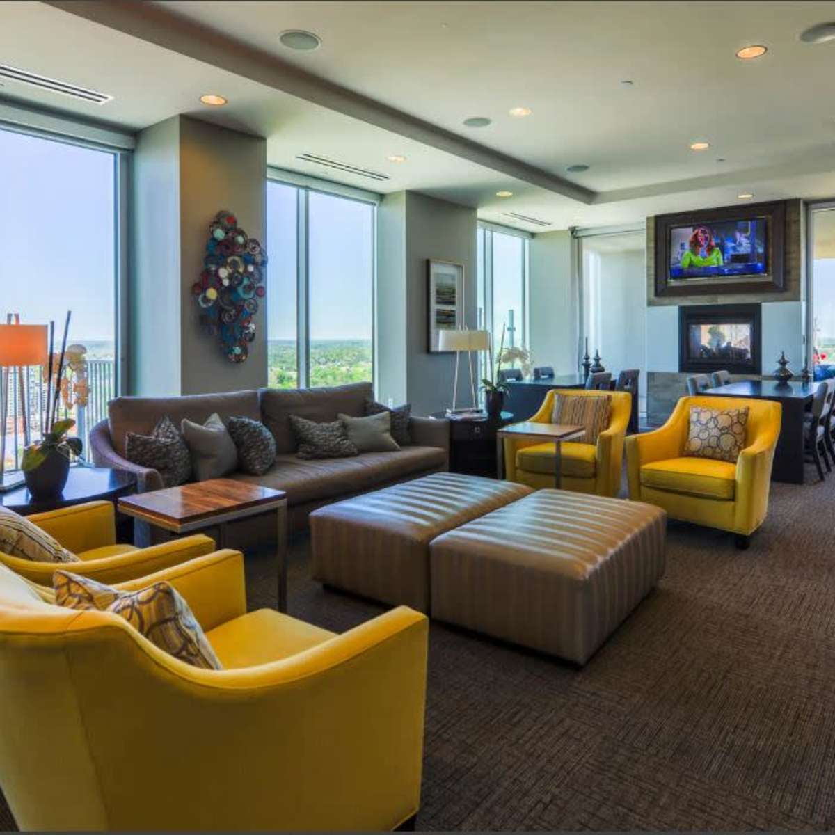 A modern living space with large windows, yellow armchairs, a sectional sofa, and a television mounted on the wall.