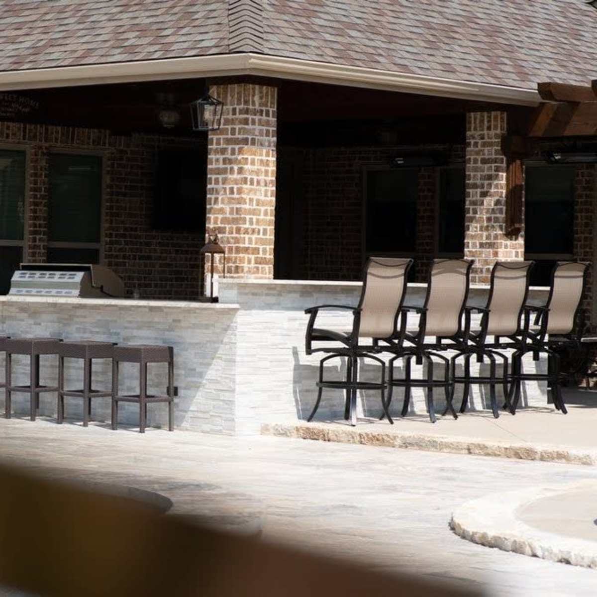 An outdoor bar area with high chairs arranged in front of a stone counter, set within a brick building.