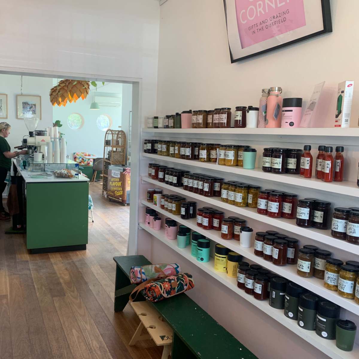 A cozy café features a counter with a barista, while shelves display jars of various jams and spreads along one wall.