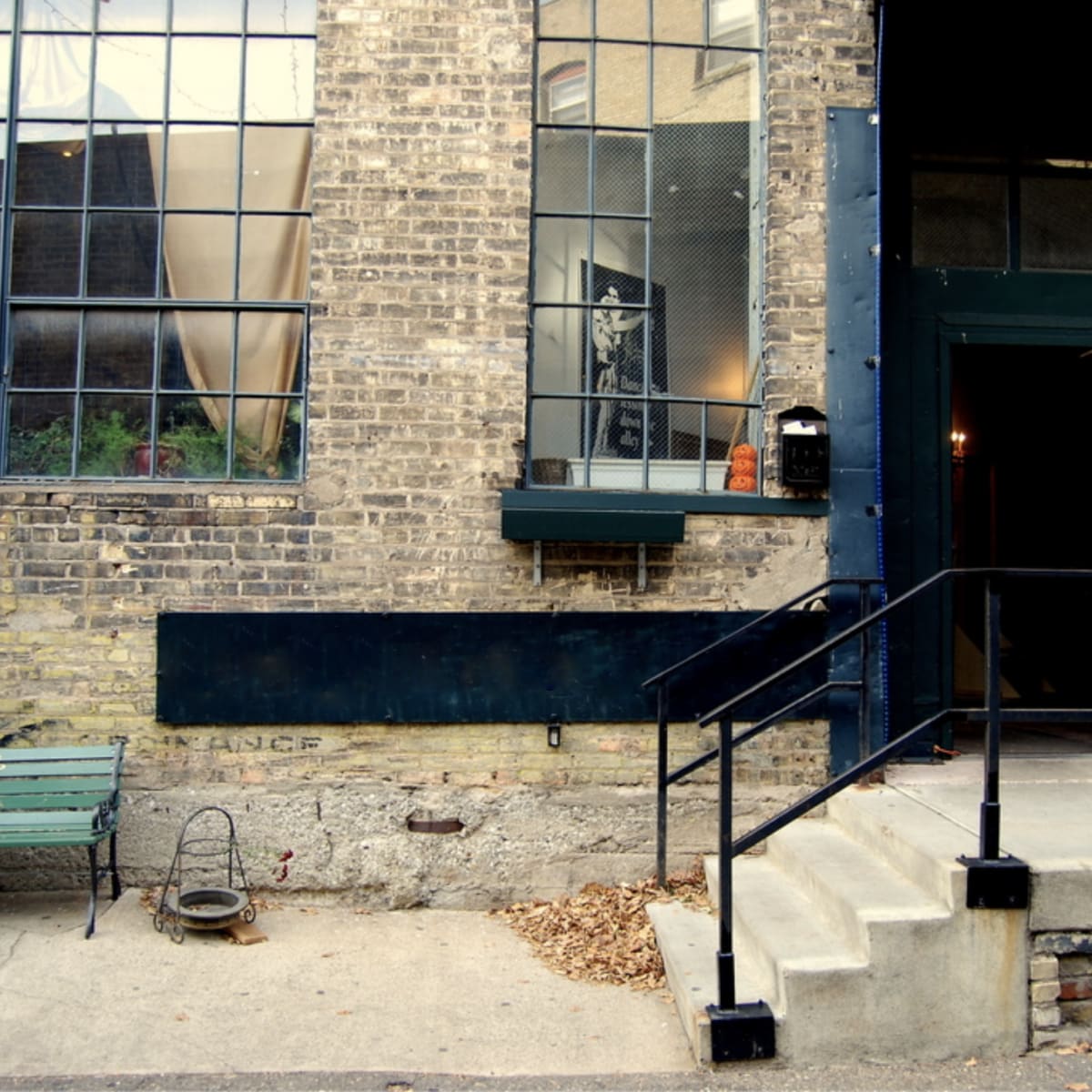A brick building features large windows, a green bench, and a set of steps leading to a dark green entrance.