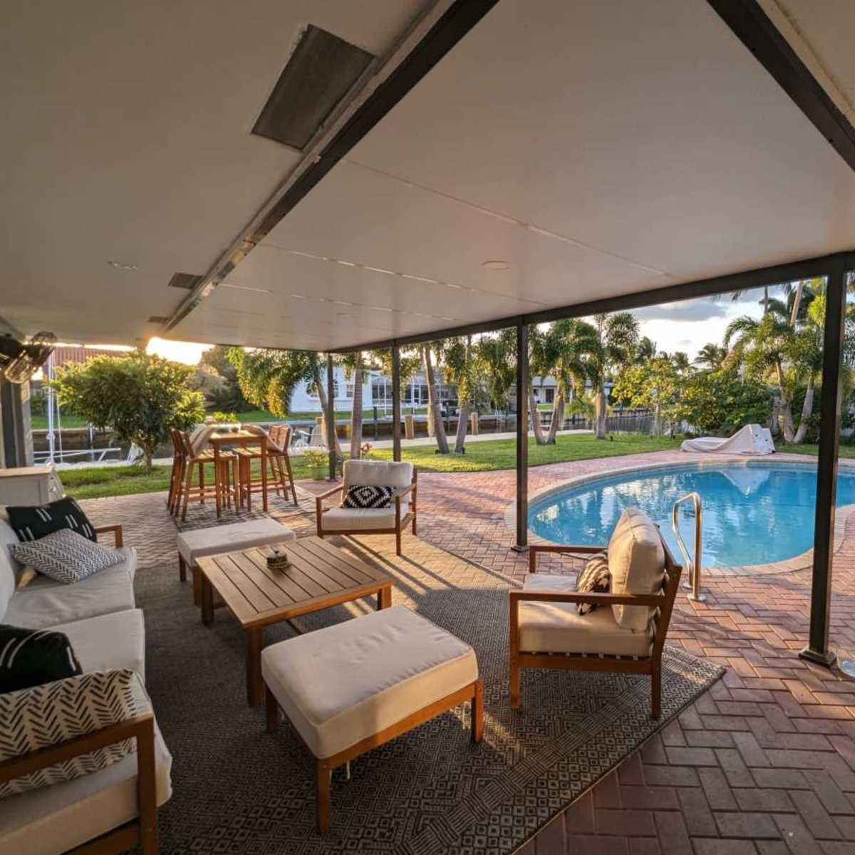 A covered outdoor lounge area with wooden furniture and a swimming pool surrounded by greenery is visible.
