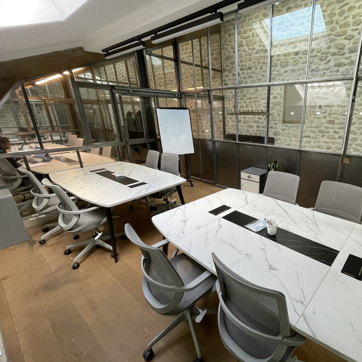 A modern office space featuring glass-walled meeting rooms with marble-topped tables and ergonomic chairs.