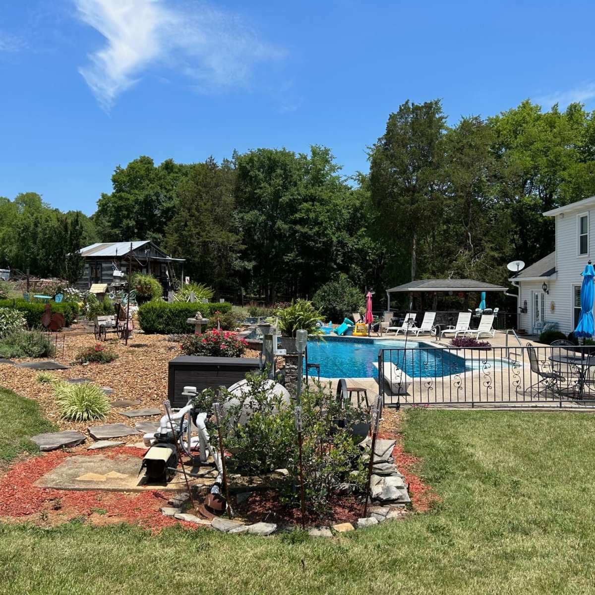 A landscaped backyard with a swimming pool, surrounded by greenery, garden beds, and outdoor seating areas.