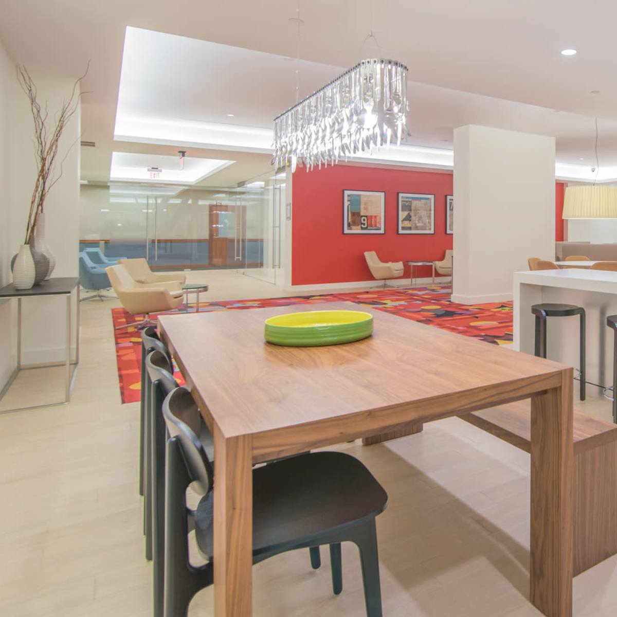 A modern kitchen and dining area features a wooden table with black chairs, a sleek island with a sink, and bright red accents on the walls.