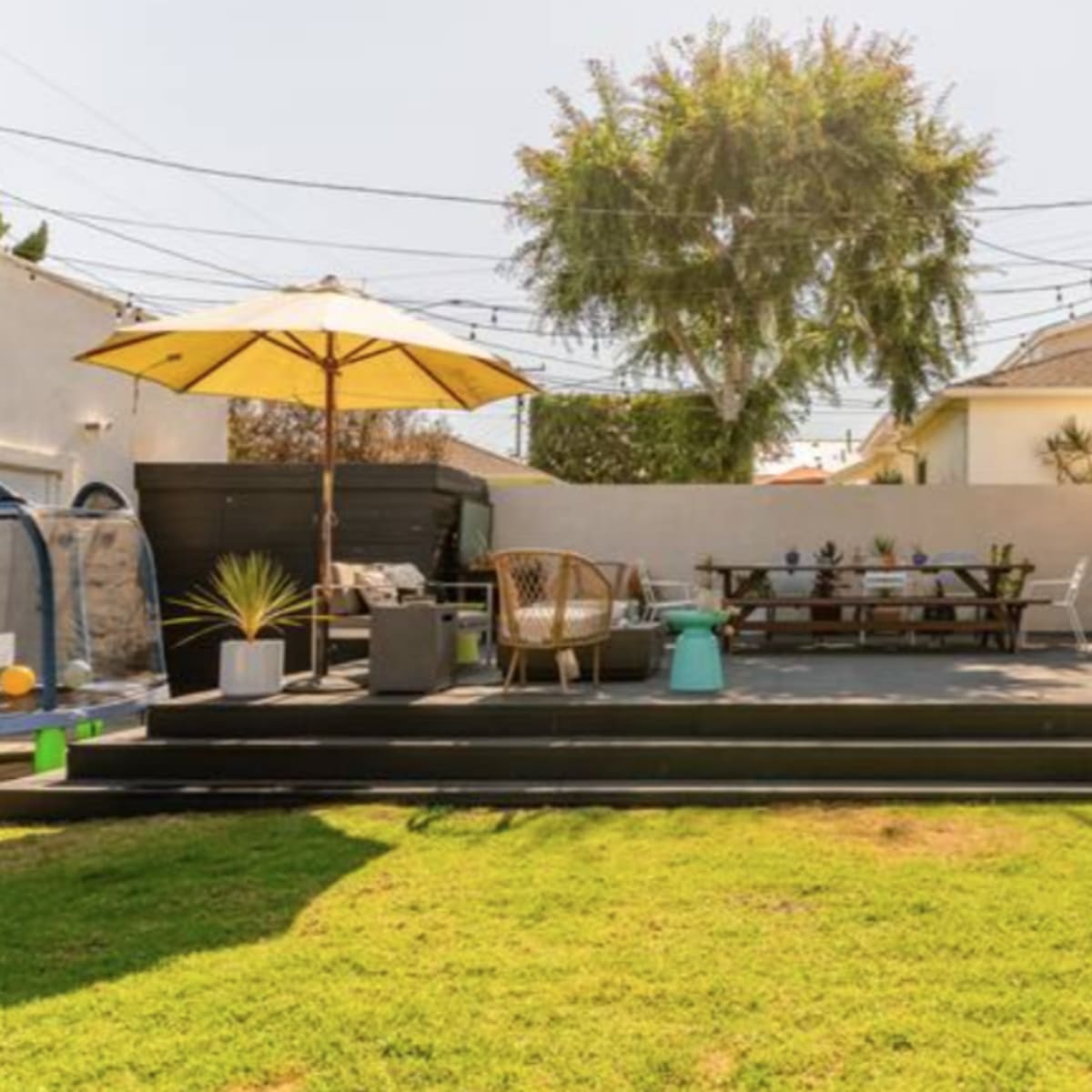 A backyard featuring a patio with seating, a dining table under an umbrella, and a well-maintained lawn.