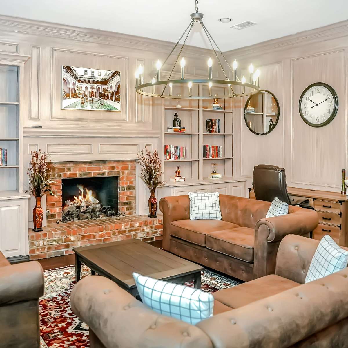 A cozy living room featuring a brick fireplace, two brown leather sofas, a wooden coffee table, and built-in bookshelves filled with various books and decor.