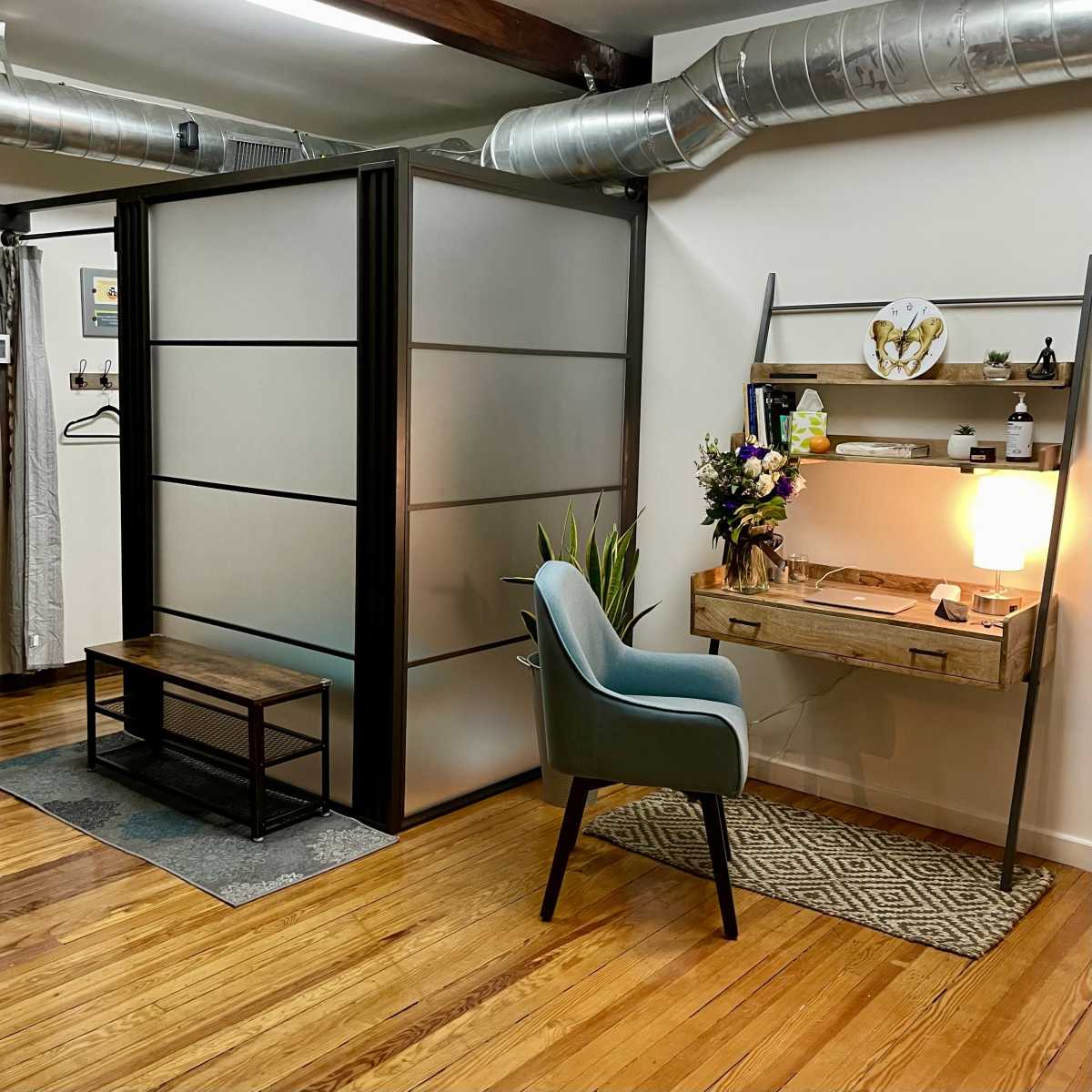 A modern office space featuring a partitioned area with a desk, chair, and decorative elements against a backdrop of wooden flooring and industrial-style ductwork.