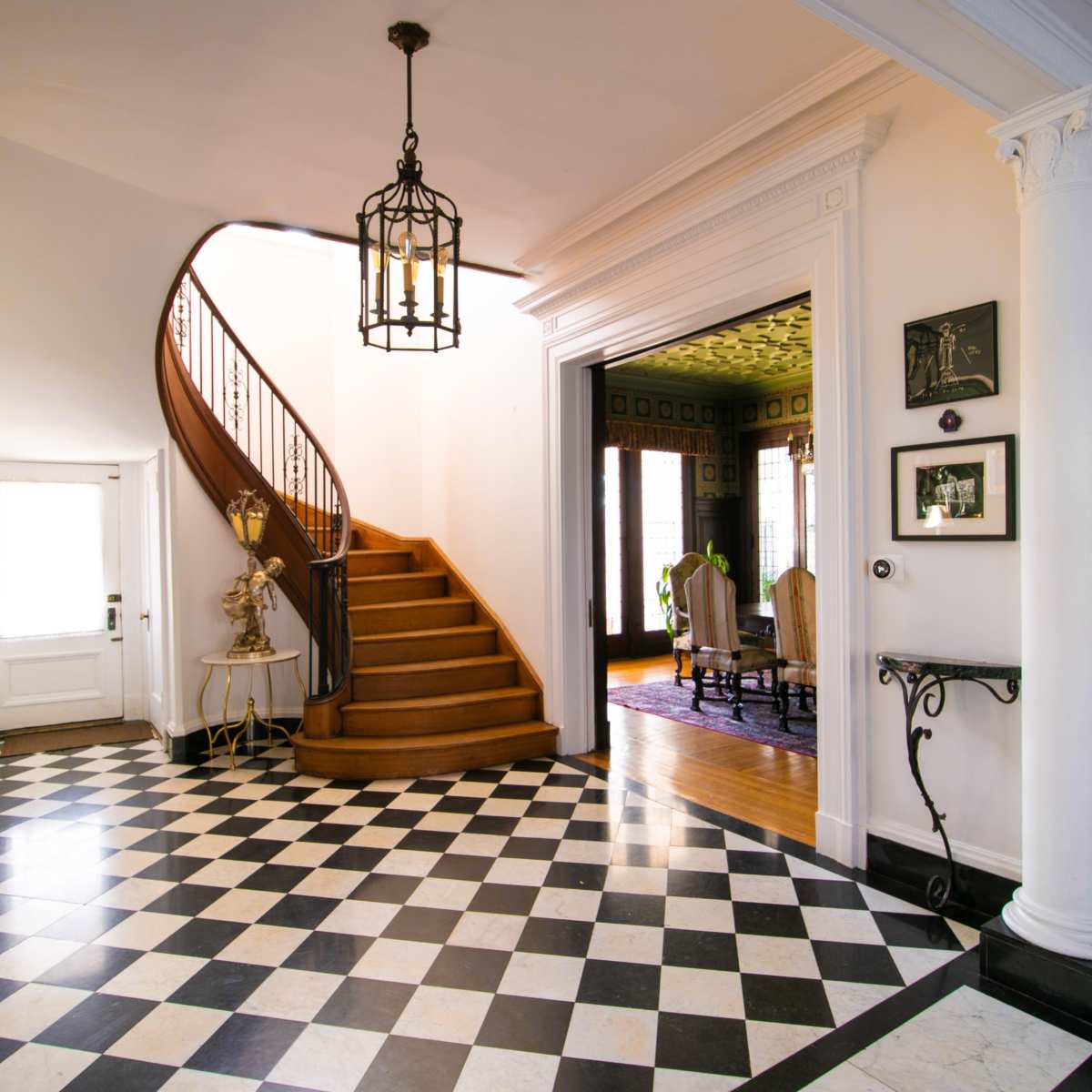 A well-lit entryway featuring a staircase with a wooden railing, black and white checkered tile flooring, and doorways leading to other rooms.
