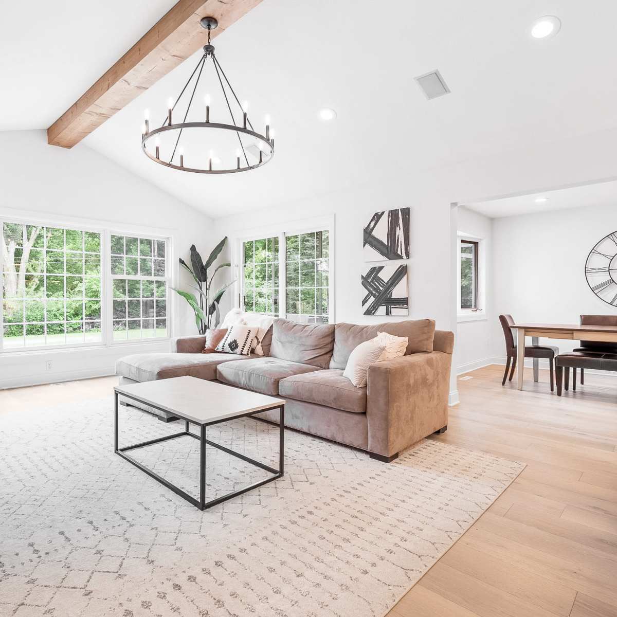 A modern living room with a sectional sofa, a coffee table, and large windows overlooking greenery.