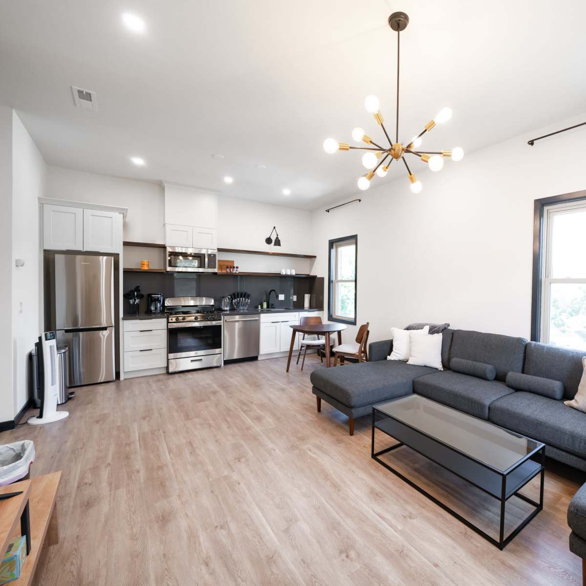 A modern living room with a sectional sofa, a coffee table, and a kitchen area featuring stainless steel appliances.