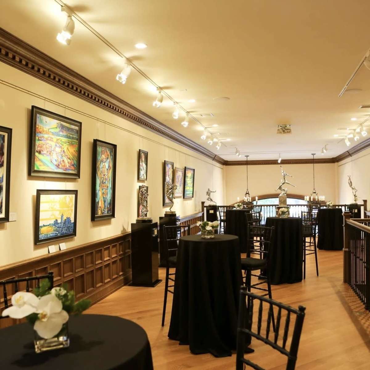 An art gallery with framed paintings displayed on the walls and small tables arranged throughout the space.