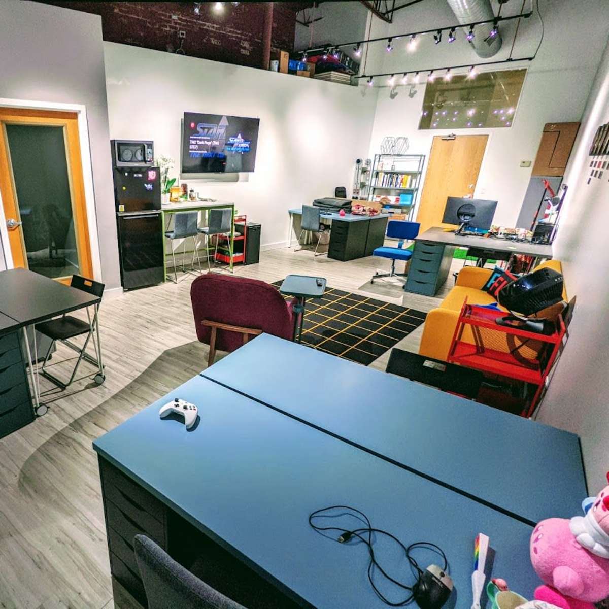 A modern office space with desks, chairs, and a television, arranged in a bright, open layout.