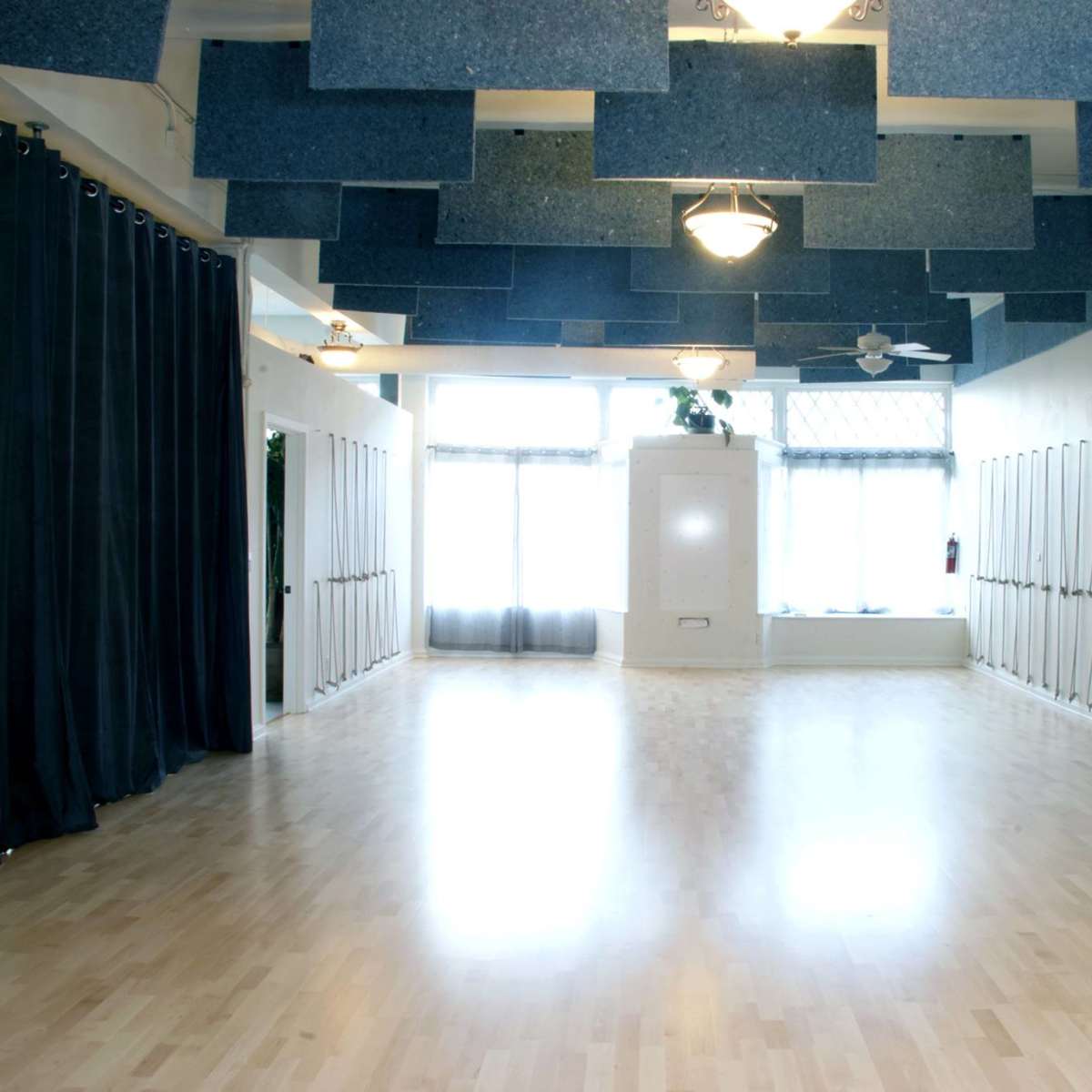 A spacious, well-lit studio with wooden flooring and blue acoustic panels on the ceiling.