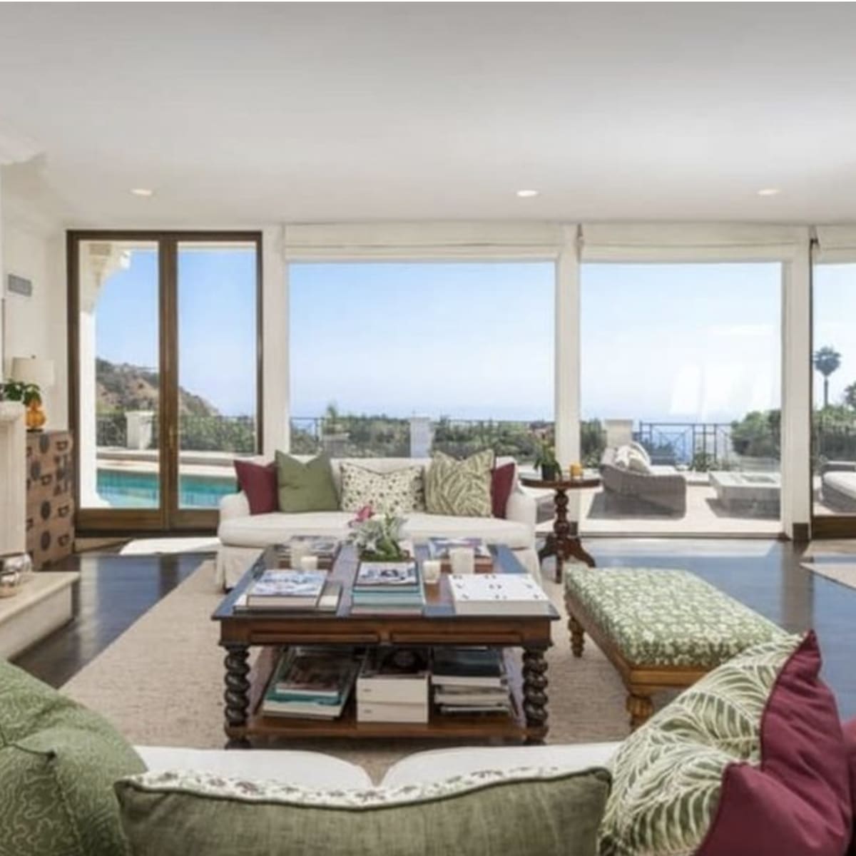 The living room features a cozy seating area with a coffee table, large windows showcasing a view of the pool and outdoor scenery.