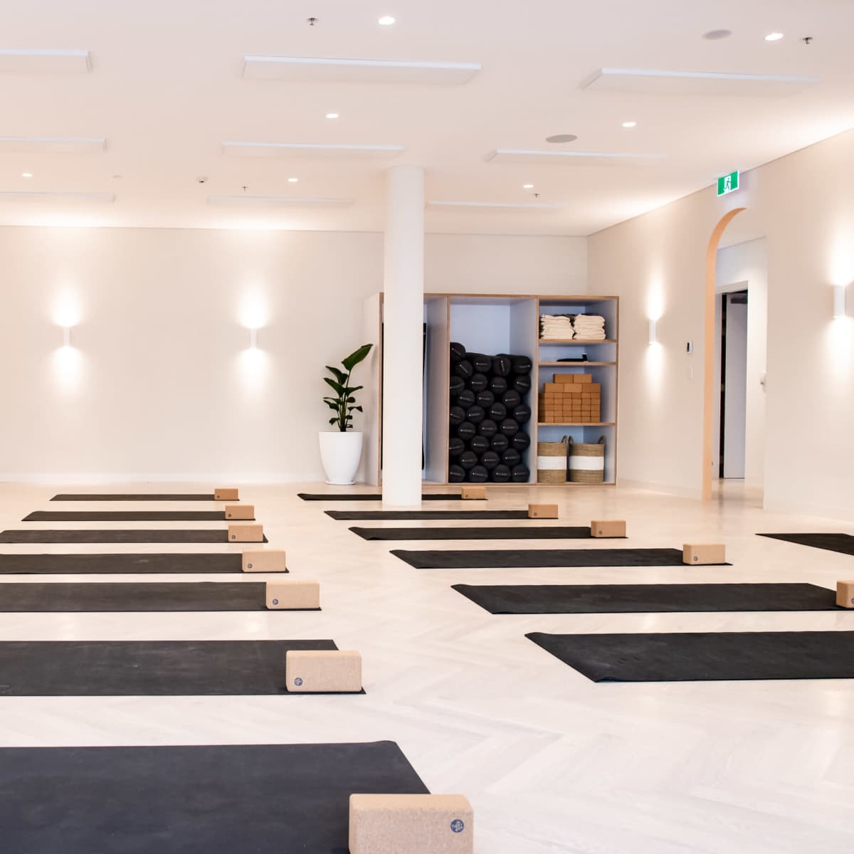 A yoga studio with neatly arranged black mats, cork blocks, and a shelf of rolled mats, illuminated by soft overhead lighting.