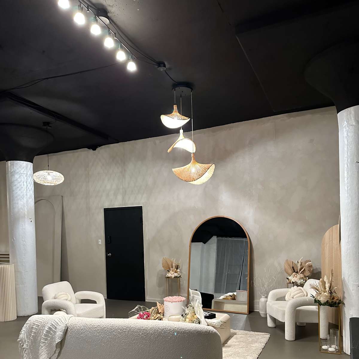A modern interior space featuring a curved white sofa, two matching armchairs, a round mirror, and decorative elements on a light-colored wall.
