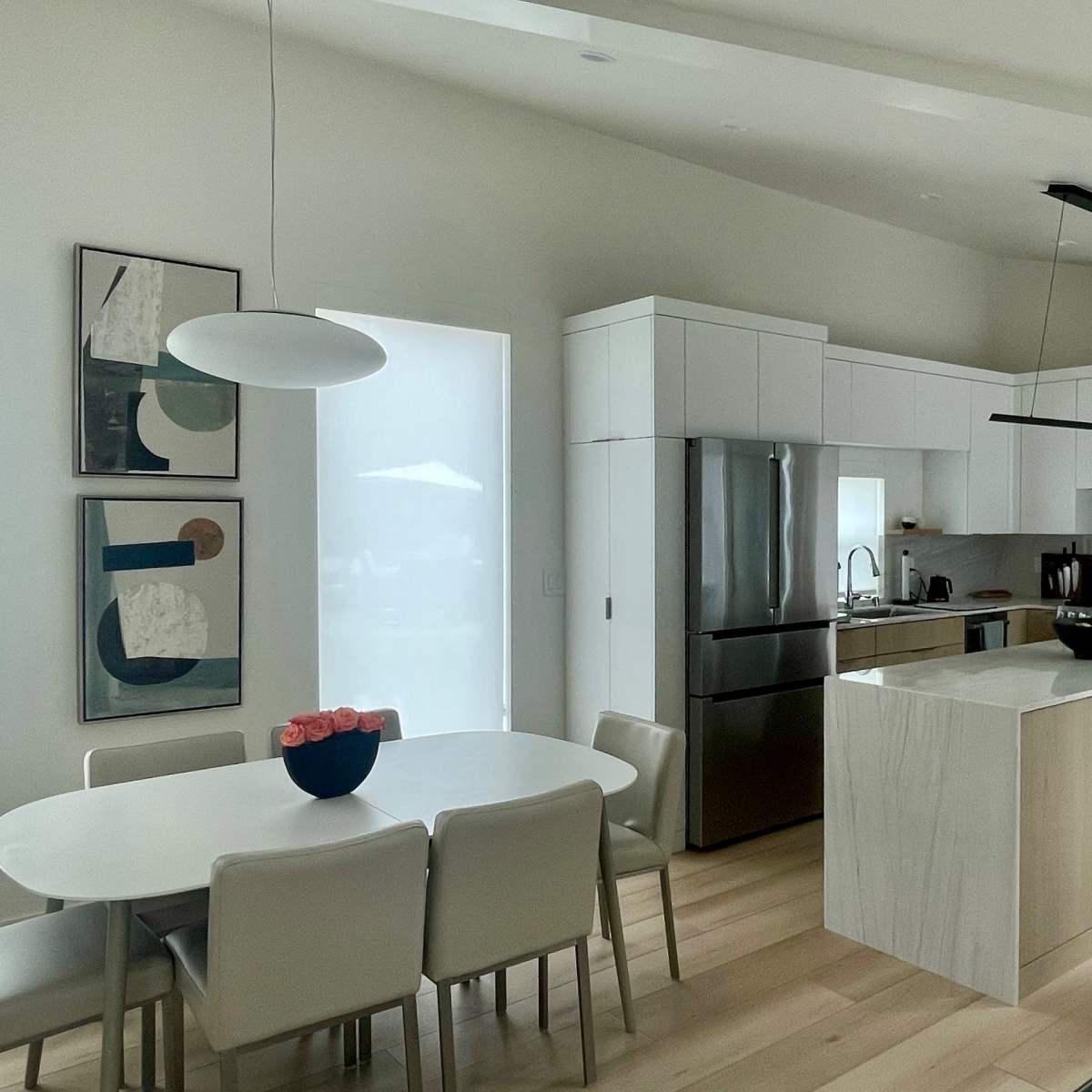 A modern kitchen with a central island, stainless steel appliances, and a dining area featuring a round table and six chairs.