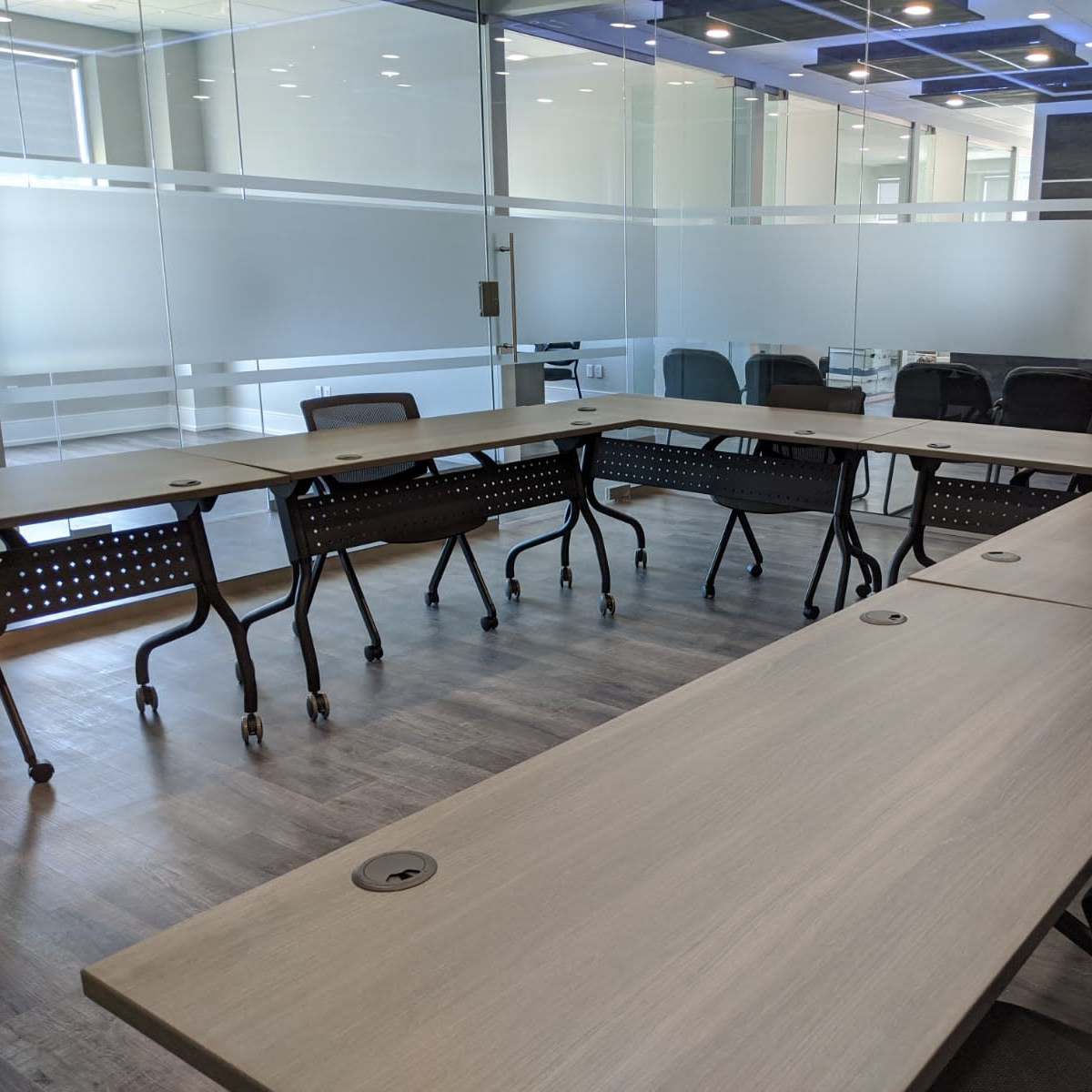 A modern conference room features a large rectangular table surrounded by multiple rolling chairs and a glass wall that provides visibility to adjacent spaces.