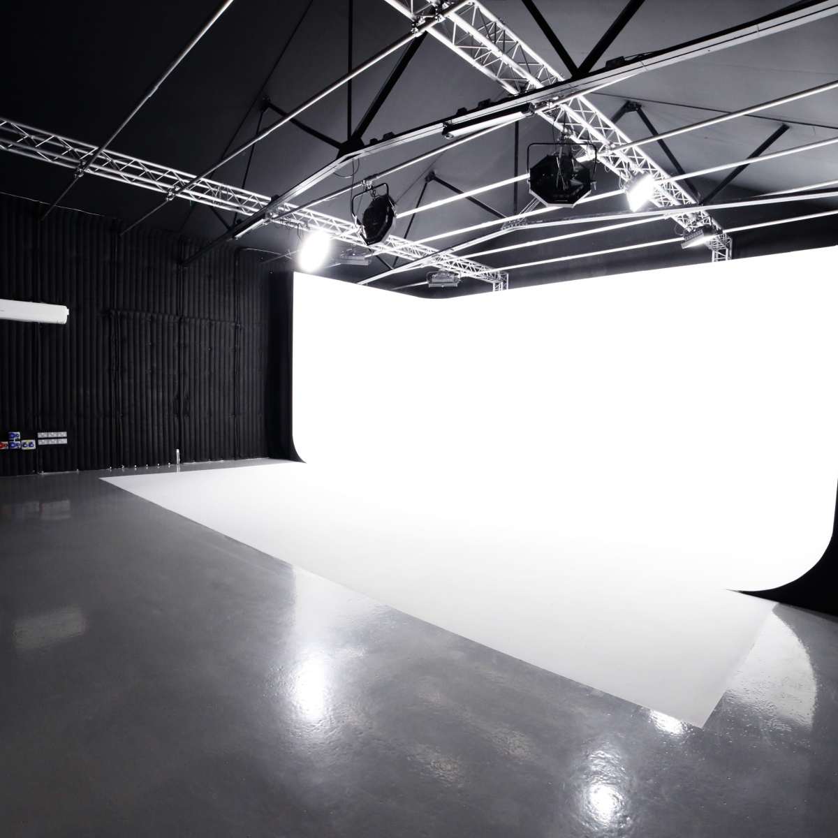 A photography studio features a large white backdrop, high ceilings, and overhead lighting.