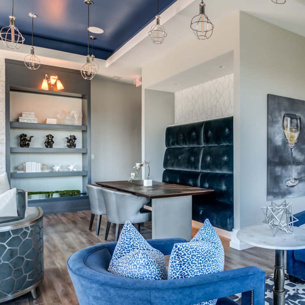 A modern lounge area featuring plush blue chairs, a dining table, and a wine refrigerator against a backdrop of stylish decor.