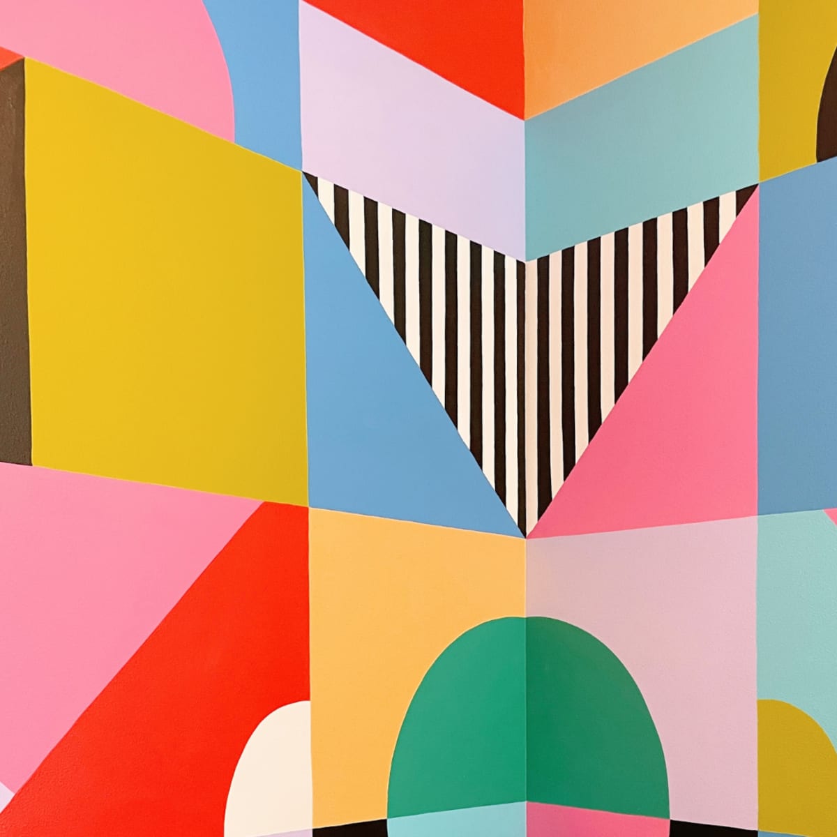 A colorful geometric mural with various shapes and vibrant hues across a wall in a corner.