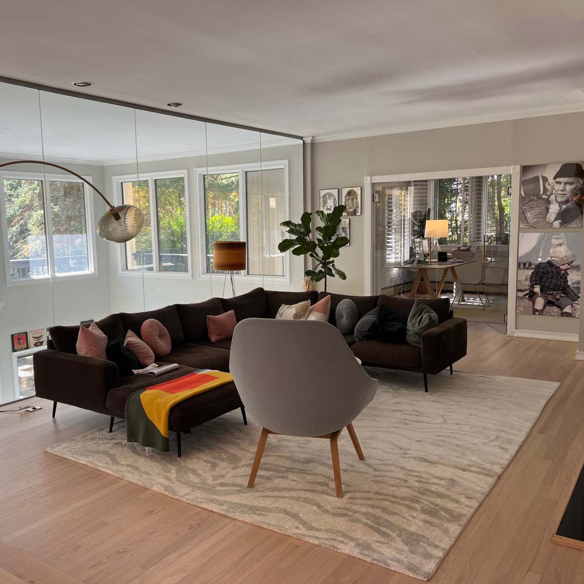 A modern living room featuring a large sectional sofa, a curved chair, a floor lamp, and large windows that provide natural light, with framed photographs on the walls.