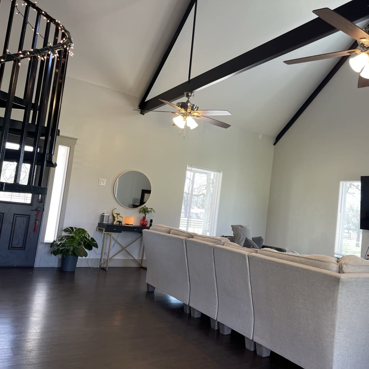 A spacious living room features a sectional sofa, a large wall-mounted television, and ceiling fans, with a spiral staircase in the corner.