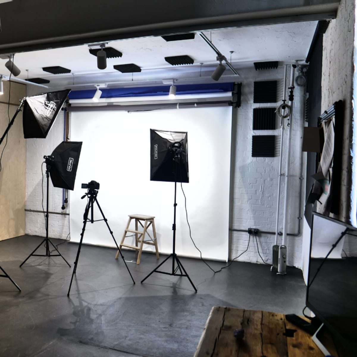 A photo studio setup features a stool, a camera on a tripod, and three lighting fixtures arranged around a backdrop.
